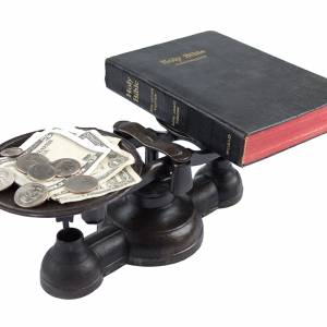 An old cast balance scale on white background balancing money versus a bible.