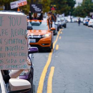 Passenger in car holding sign that reads: If you are neutral in situations of injustice, you have chosen the side of the oppressor.