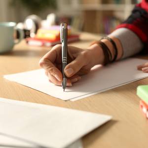 Person writing a letter with a pen