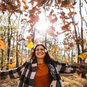 Smiling woman with arms outstretched as leaves are blowing all around her