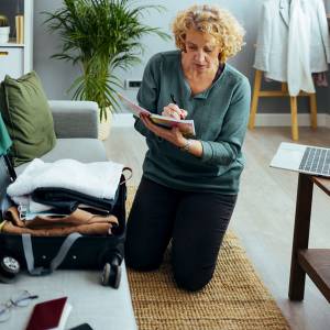 Woman packing her suitcase and checking off packed items on her list