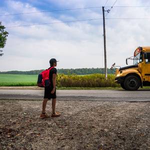 Child of color waits for a school bus in a rural area.