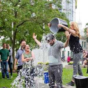 Woman pours a bucket of water over a man’s head during a fundraiser