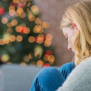 Depressed woman sits next to a Christmas tree.