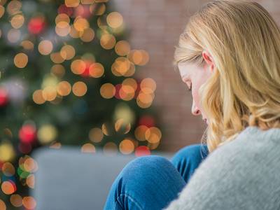 Depressed woman sits next to a Christmas tree.